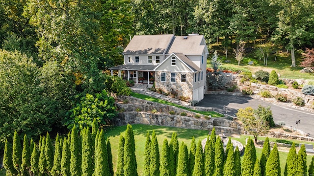 view of front of house with roof with shingles, a front lawn, stone siding, a porch, and driveway
