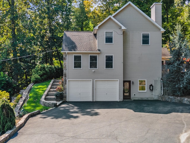 view of side of home featuring a garage, a chimney, and driveway