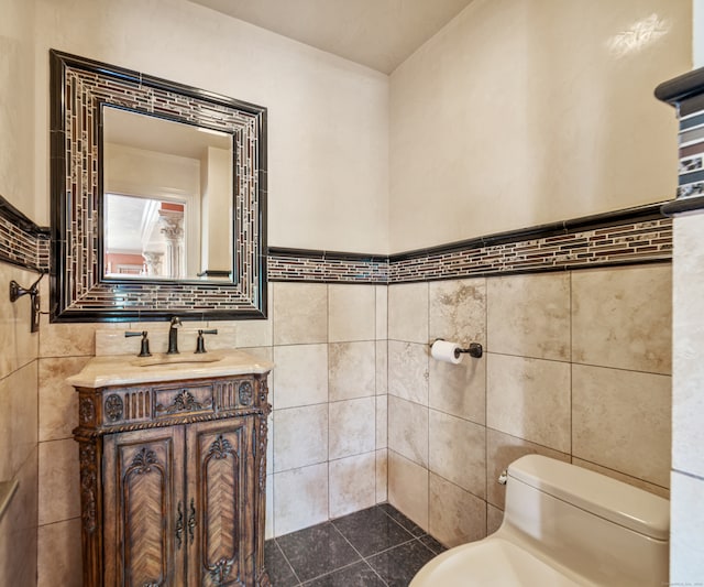 bathroom featuring vanity, a wainscoted wall, toilet, and tile walls