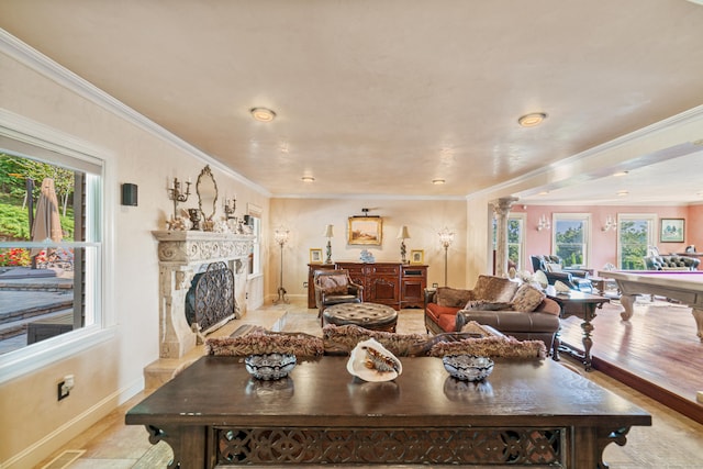 living room featuring a fireplace with raised hearth, baseboards, ornamental molding, and a healthy amount of sunlight