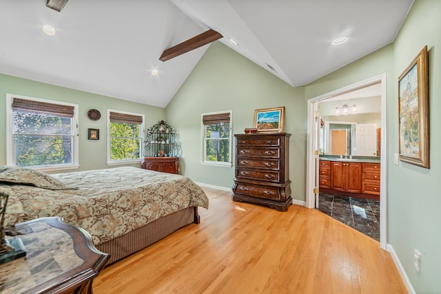 bedroom featuring ceiling fan, beam ceiling, light hardwood / wood-style flooring, high vaulted ceiling, and ensuite bath