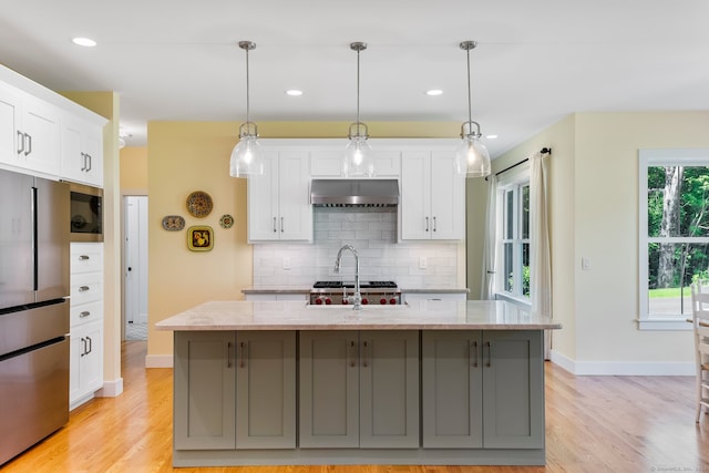 kitchen featuring light stone countertops, a kitchen island with sink, hanging light fixtures, stainless steel refrigerator, and white cabinets