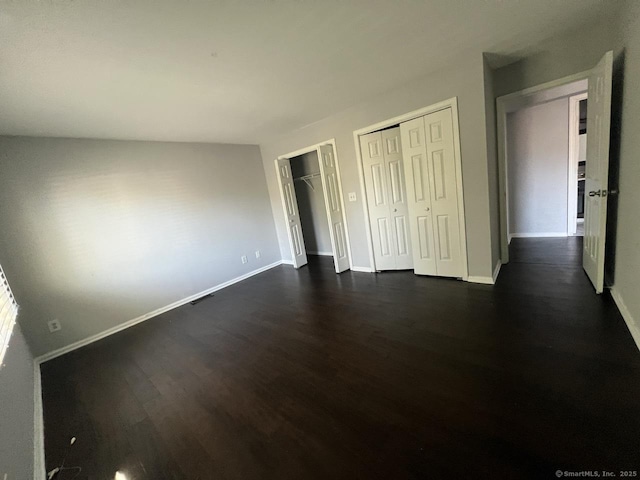 unfurnished bedroom featuring two closets, dark wood-style flooring, and baseboards