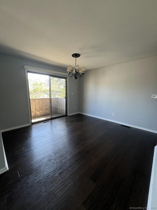 unfurnished room with dark wood-type flooring, baseboards, a notable chandelier, and visible vents