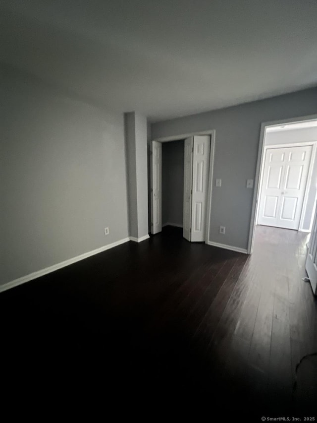 unfurnished bedroom featuring baseboards, dark wood finished floors, and a closet
