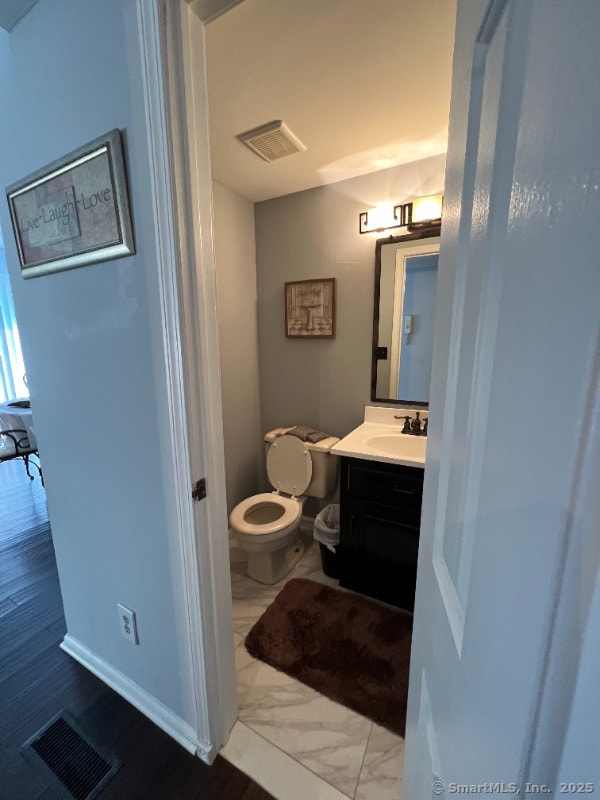 half bath featuring visible vents, toilet, and vanity