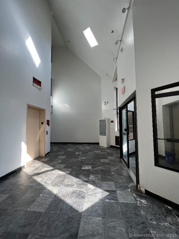 corridor featuring track lighting, high vaulted ceiling, and baseboards