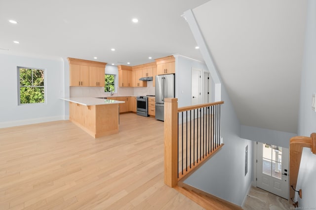 kitchen featuring appliances with stainless steel finishes, light hardwood / wood-style floors, light brown cabinets, kitchen peninsula, and a kitchen bar