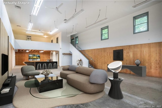 living room with concrete floors, wood walls, a towering ceiling, and indoor bar