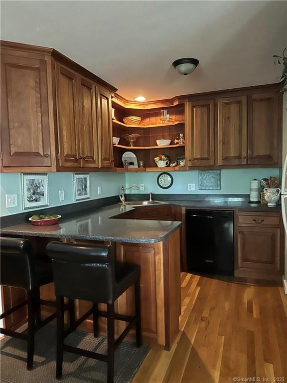 kitchen featuring black dishwasher, a kitchen bar, kitchen peninsula, sink, and hardwood / wood-style flooring