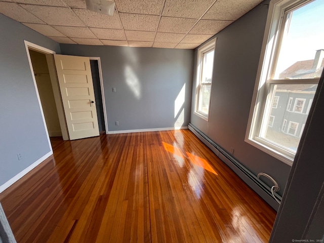 unfurnished bedroom featuring a baseboard heating unit, a paneled ceiling, and wood-type flooring