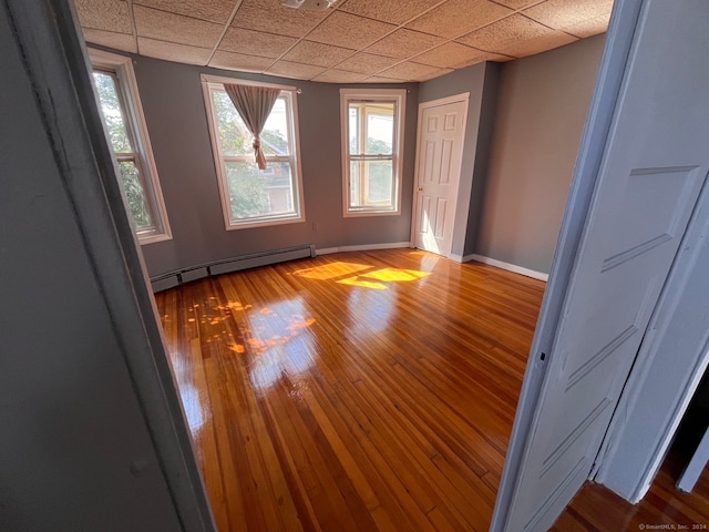 unfurnished room with hardwood / wood-style flooring, baseboard heating, and a drop ceiling