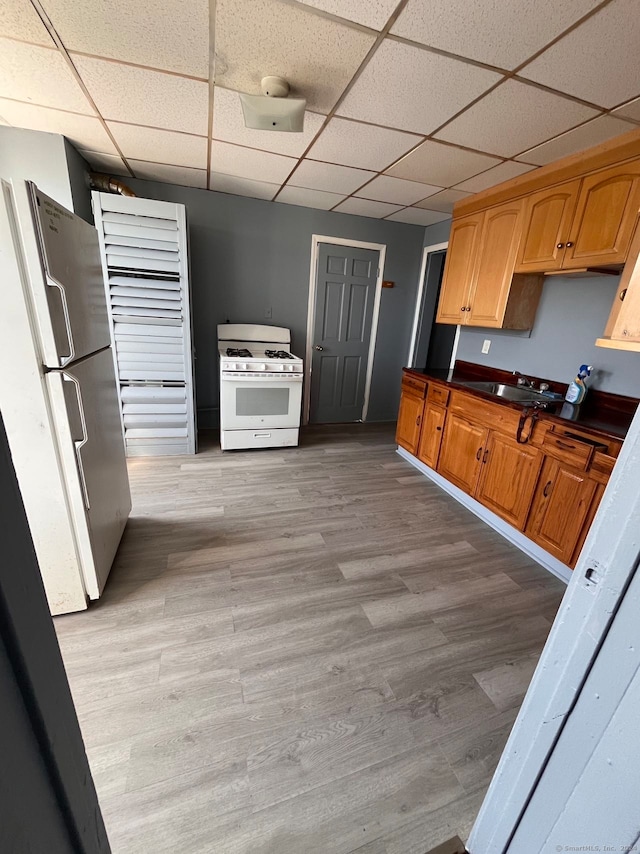 kitchen featuring white range with gas cooktop, light hardwood / wood-style flooring, stainless steel refrigerator, and a paneled ceiling