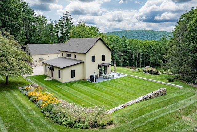 89 Under Mountain Rd, Canaan, CT 06031 - rear view of property featuring stucco siding, a patio, a lawn, and a wooded view