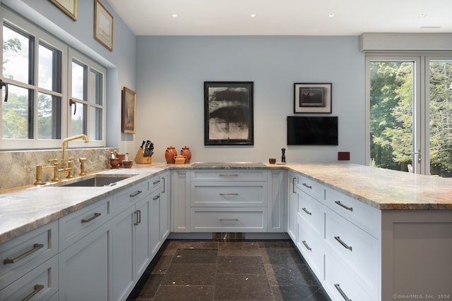 kitchen featuring light stone countertops, tasteful backsplash, kitchen peninsula, sink, and white cabinets