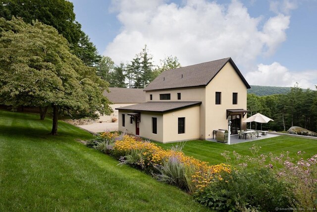 89 Under Mountain Rd, Canaan, CT 06031 - back of property with stucco siding, a patio area, a lawn, and roof with shingles
