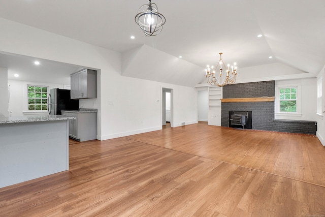 unfurnished living room with light wood-type flooring, plenty of natural light, a chandelier, and lofted ceiling