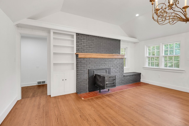 unfurnished living room featuring an inviting chandelier, lofted ceiling, hardwood / wood-style floors, and a wood stove