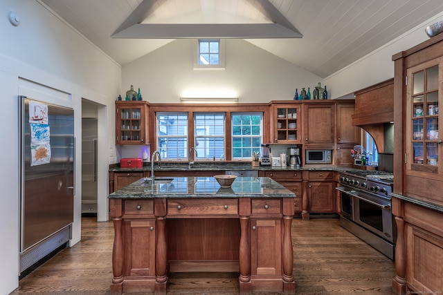 kitchen with a wealth of natural light, dark stone counters, high end appliances, and an island with sink