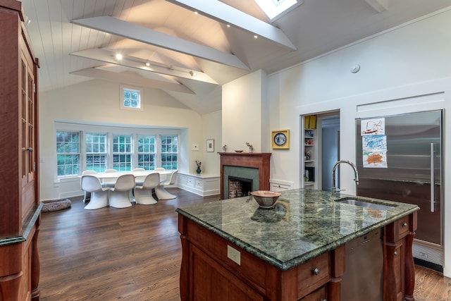 kitchen with a kitchen island with sink, dark stone counters, dark wood-type flooring, sink, and stainless steel appliances