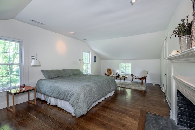 bedroom with lofted ceiling, dark wood-type flooring, and a brick fireplace