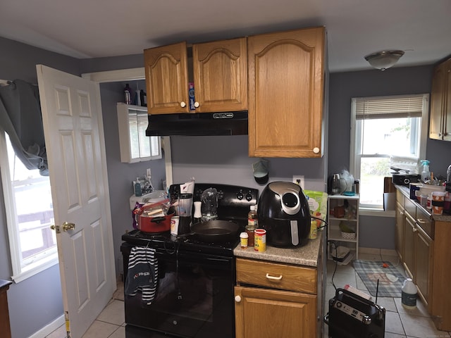 218 Oak Ave, Torrington, CT 06790 - kitchen with under cabinet range hood, light tile patterned floors, brown cabinetry, black / electric stove, and light countertops