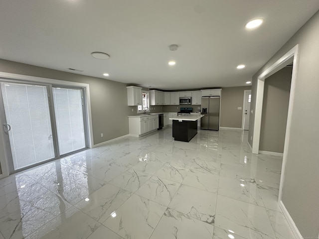 kitchen featuring a center island, sink, appliances with stainless steel finishes, white cabinetry, and a breakfast bar area