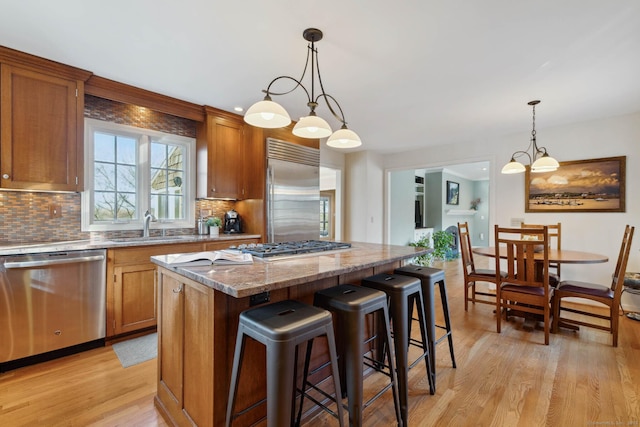 kitchen with appliances with stainless steel finishes, sink, pendant lighting, light hardwood / wood-style flooring, and a center island