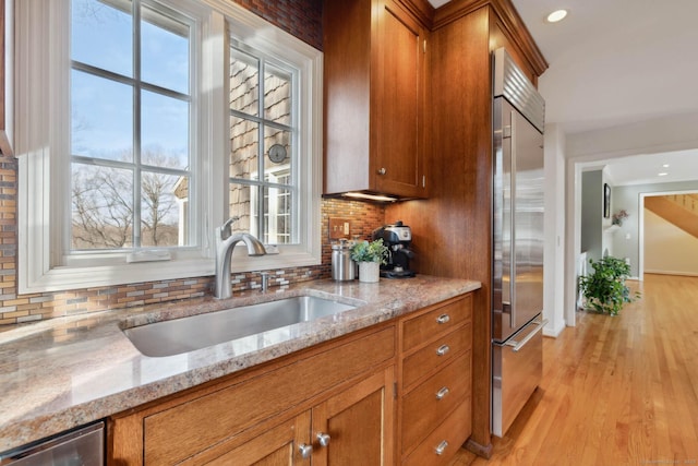 kitchen with sink, stainless steel appliances, tasteful backsplash, light stone counters, and light wood-type flooring