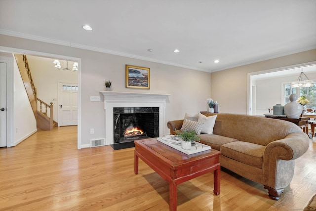 living room featuring light wood-type flooring, a premium fireplace, crown molding, and an inviting chandelier