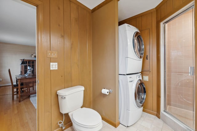 bathroom with toilet, stacked washing maching and dryer, and walk in shower