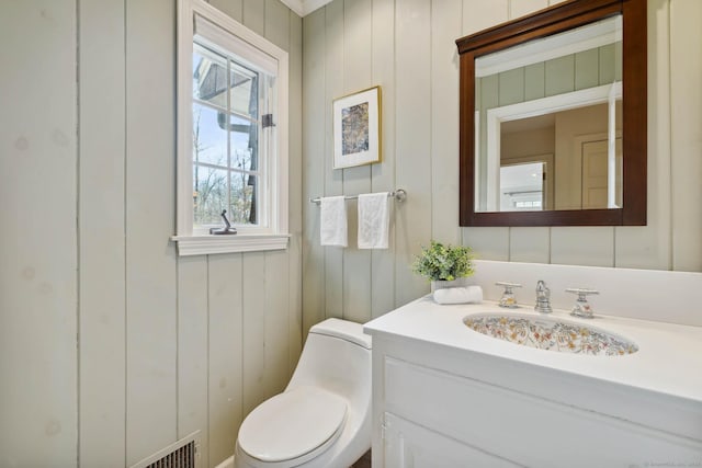 bathroom featuring vanity, toilet, and wooden walls