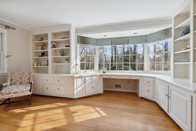 unfurnished office featuring light hardwood / wood-style floors, built in desk, and crown molding