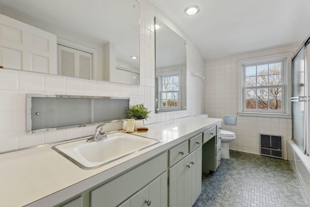 full bathroom with bath / shower combo with glass door, vanity, tile walls, tile patterned flooring, and toilet