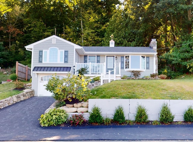 split level home featuring fence, a front yard, a chimney, an attached garage, and driveway