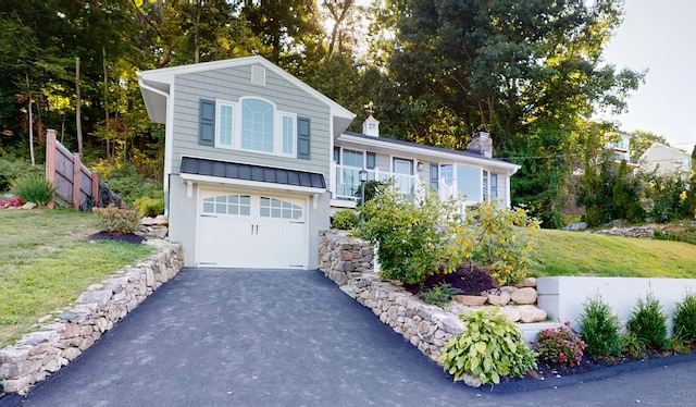 split level home featuring an attached garage, aphalt driveway, a front yard, a chimney, and a standing seam roof