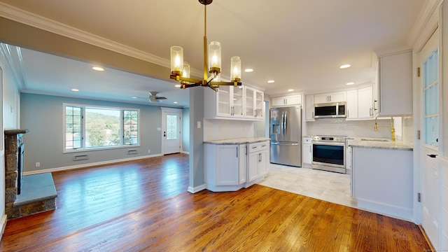 kitchen with light wood-type flooring, ceiling fan with notable chandelier, stainless steel appliances, crown molding, and white cabinets