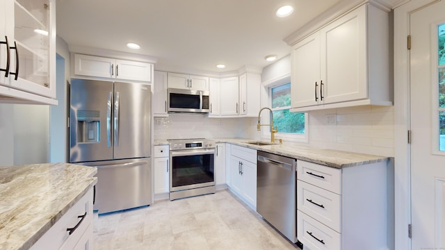 kitchen with white cabinets, light stone counters, a sink, stainless steel appliances, and tasteful backsplash