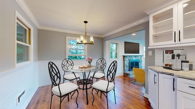 dining room featuring a stone fireplace, dark hardwood / wood-style flooring, ornamental molding, and an inviting chandelier