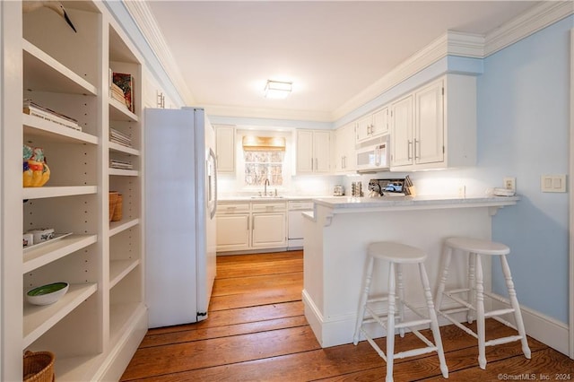 kitchen with a kitchen breakfast bar, white appliances, light hardwood / wood-style flooring, sink, and white cabinetry