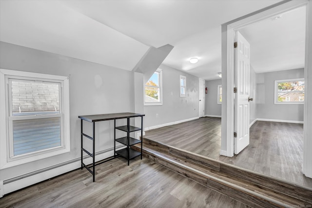 additional living space featuring wood-type flooring, a baseboard heating unit, and plenty of natural light