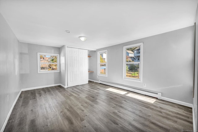 unfurnished bedroom featuring a closet, hardwood / wood-style flooring, multiple windows, and a baseboard heating unit