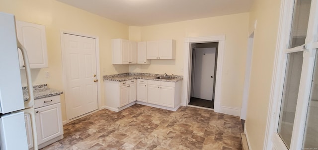 kitchen with light stone countertops, baseboards, freestanding refrigerator, a sink, and white cabinets