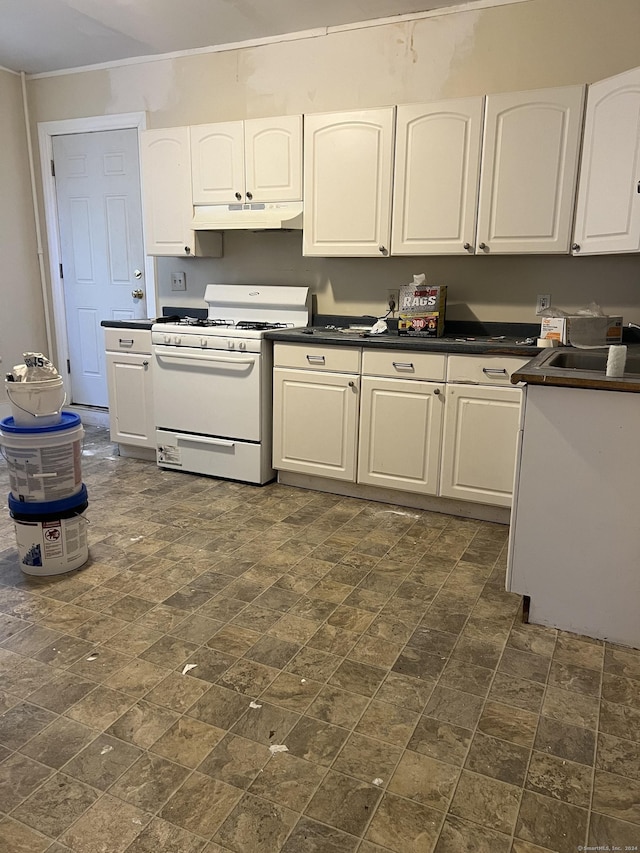 kitchen with under cabinet range hood, a sink, dark countertops, white gas range oven, and white cabinets