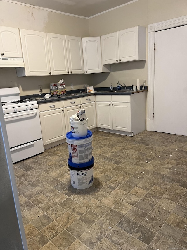 kitchen featuring dark countertops, under cabinet range hood, ornamental molding, white gas range oven, and white cabinetry