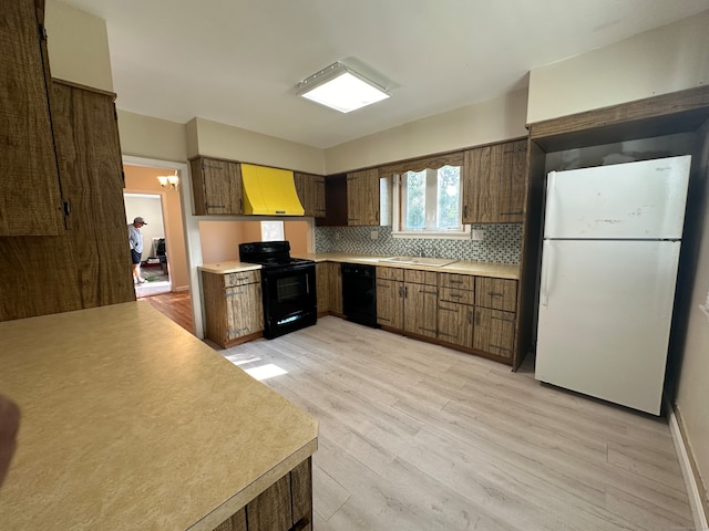 kitchen with light wood-type flooring, backsplash, black appliances, premium range hood, and sink