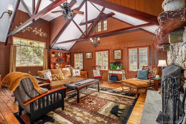 living room with wood walls, beamed ceiling, a fireplace, hardwood / wood-style floors, and ceiling fan