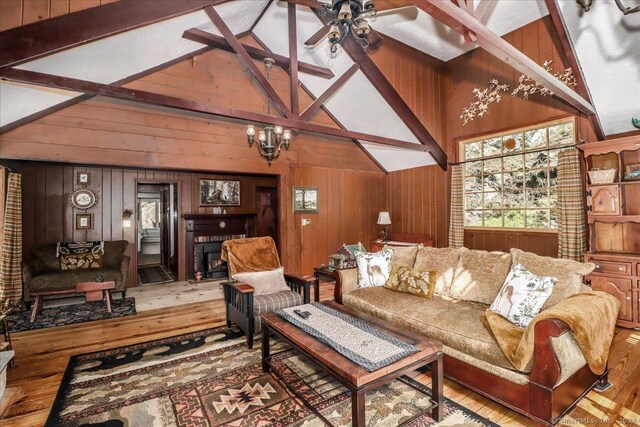 living room featuring ceiling fan with notable chandelier, lofted ceiling with beams, hardwood / wood-style flooring, and wooden walls