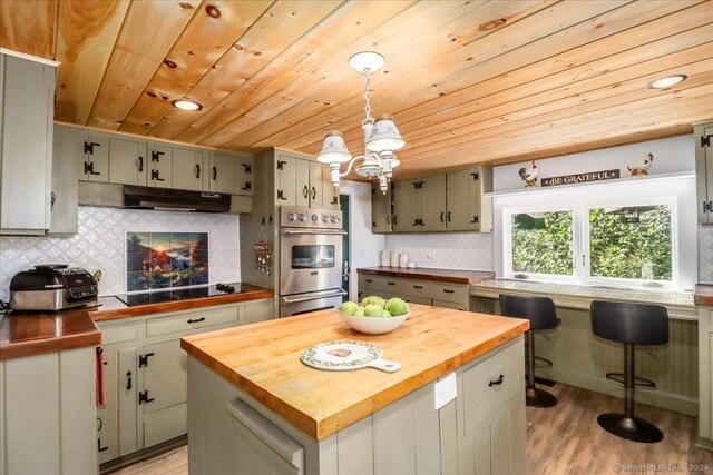 kitchen with ventilation hood, hanging light fixtures, wood ceiling, wooden counters, and black electric stovetop