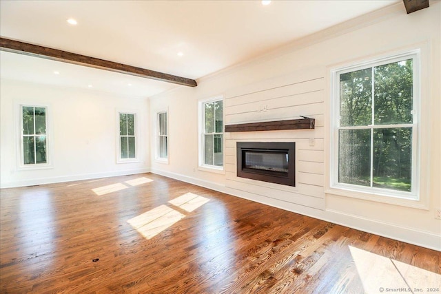 unfurnished living room with beamed ceiling, a healthy amount of sunlight, wood-type flooring, and ornamental molding